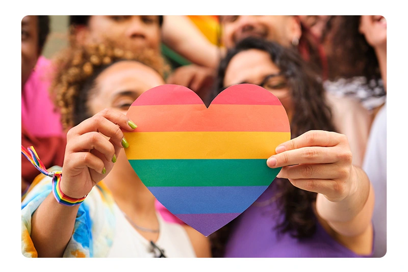 two women hold a rainbow heart together to celebrate pride month
